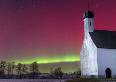 Kirche mit Polarlicht am Himmel und verschneite Landschaft.